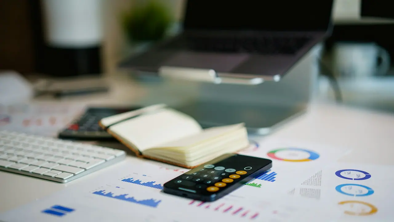 Mesa de oficina con informes financieros, gráficos, calculadora y teclado