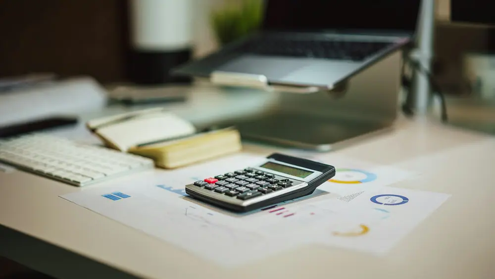 Calculadora sobre documentos con gráficos junto a un portátil
