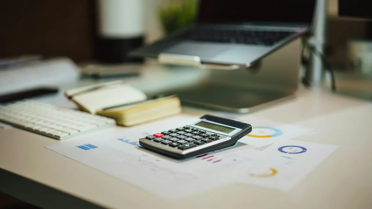 Calculadora sobre documentos con gráficos junto a un portátil